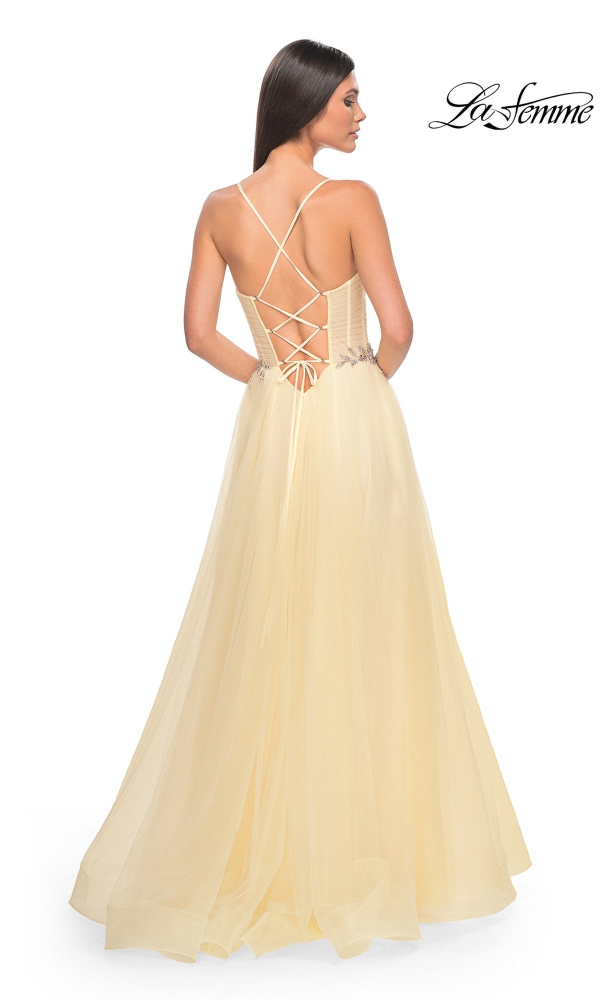 A woman models the La Femme Sheer-Bodice Long A-Line Prom Dress 32117 in light yellow, featuring an open back with crisscross lace-up details, against a plain white background.